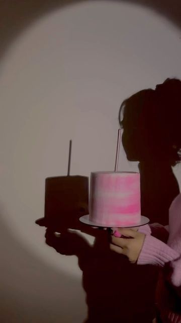 a woman holding a pink cake in front of her face and shadow on the wall