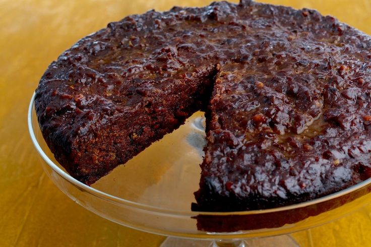 a chocolate cake with one slice missing from it on a glass platter sitting on a wooden table