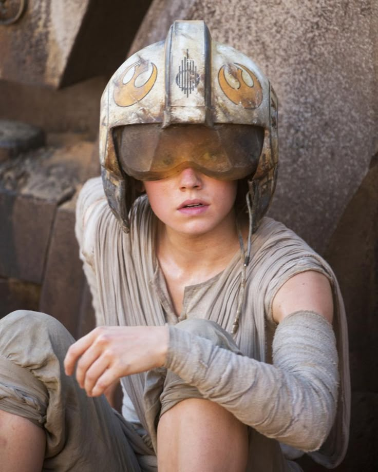 a young boy wearing a star wars helmet and sitting on the ground with his arm outstretched