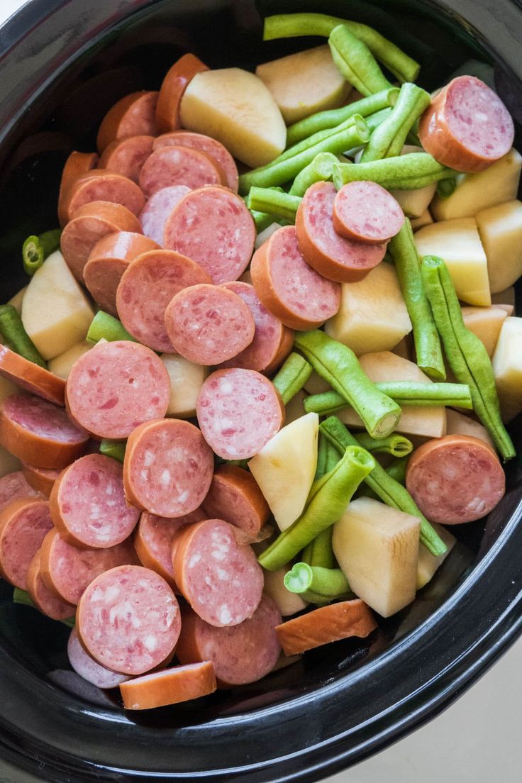 a crock pot filled with sausage, green beans and potatoes