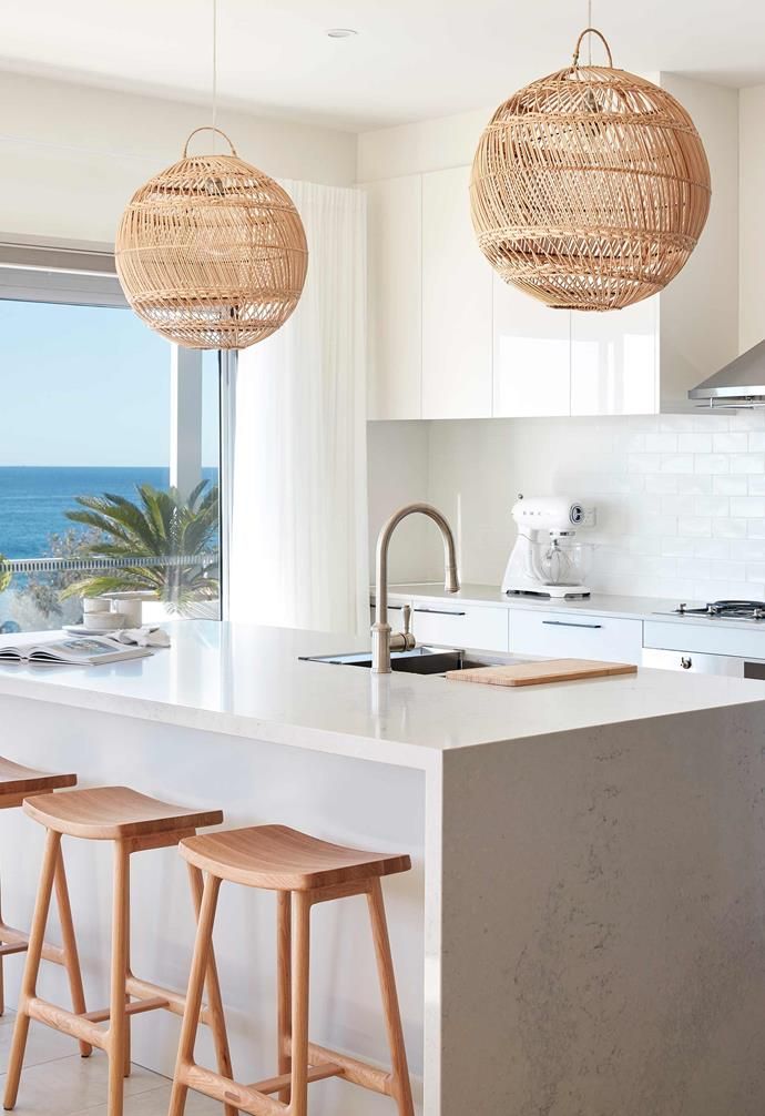 three wooden stools sit in front of an island with two hanging lights above it