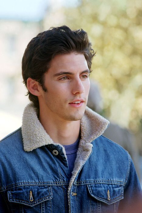 a young man in a denim jacket looks off to the side