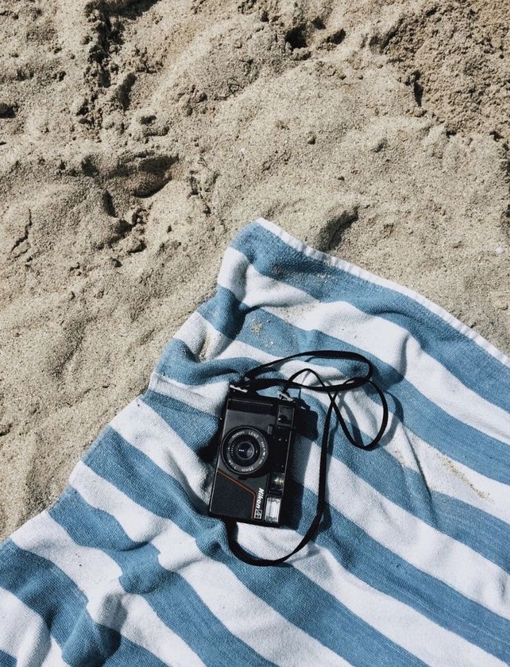 a camera sitting on top of a blue and white striped beach towel in the sand