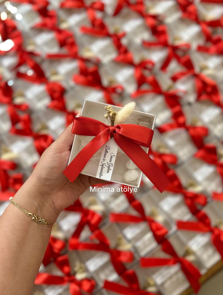 a person holding up a small box with a red ribbon on it and some other boxes in the background