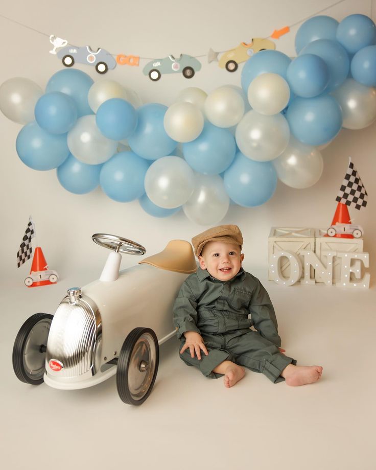 a little boy sitting on the floor in front of balloons and a plane with a name sign