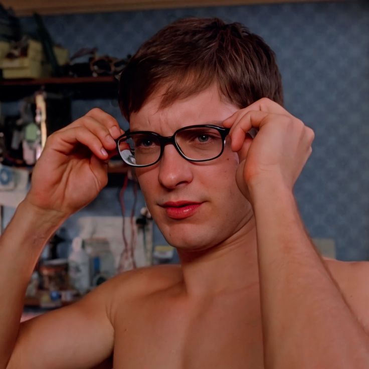 a shirtless man wearing glasses is looking at the camera while holding his hands to his temples