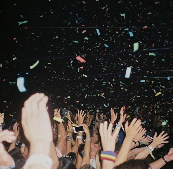 many people are holding their hands in the air and confetti is flying around them