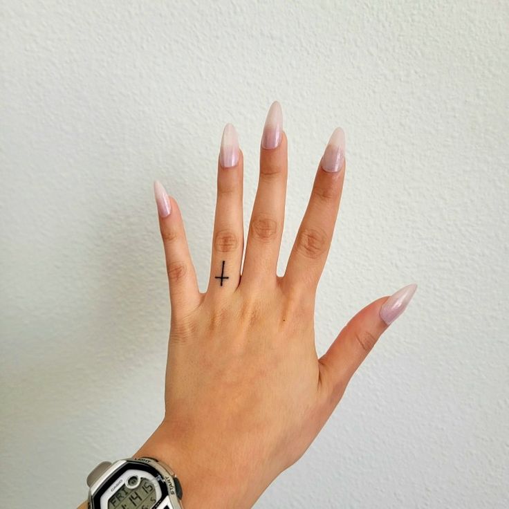 a woman's hand with white nails and a cross tattoo on her ring finger