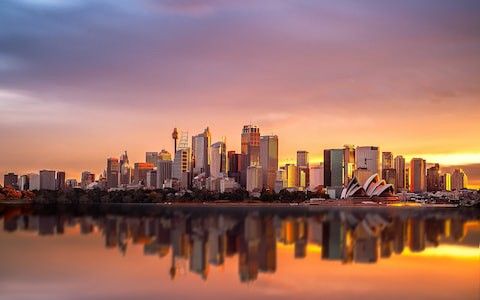 the sydney skyline is reflected in the water at sunset, with an orange and purple sky