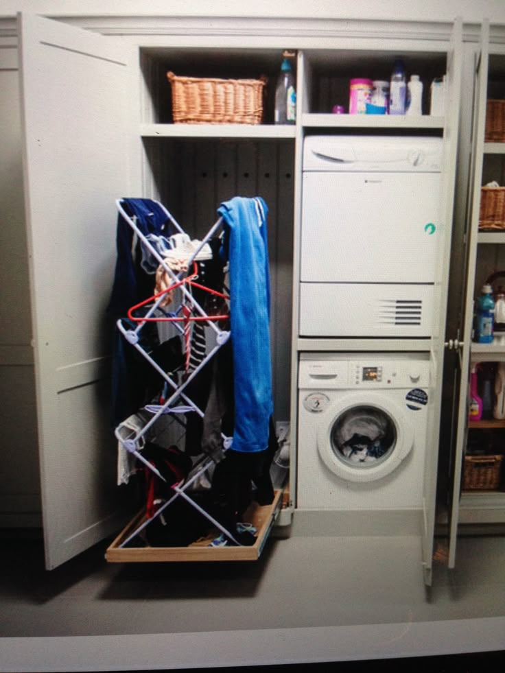 a washer and dryer sitting in a room next to an open cabinet with clothes on it