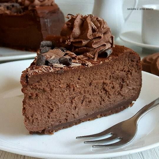 a piece of chocolate cake on a white plate with a fork and coffee mug in the background