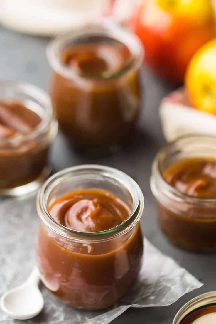 three jars filled with peanut butter sitting on top of a table next to apples and oranges