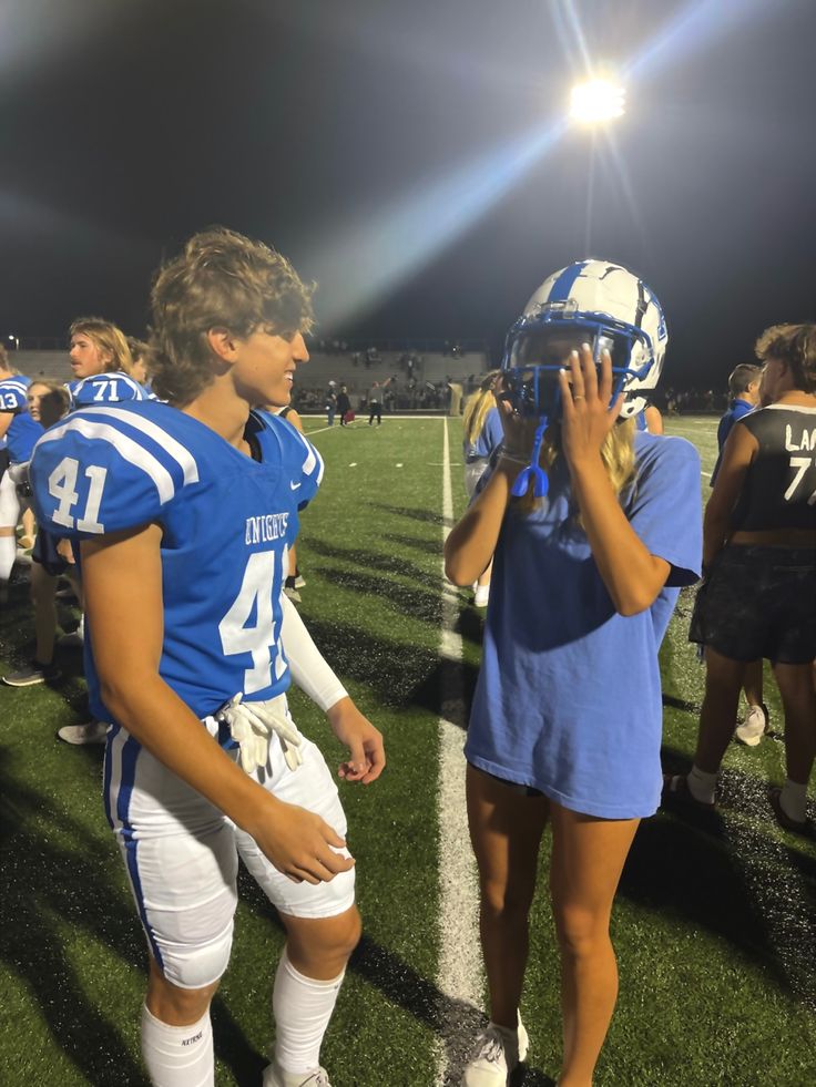 two football players standing on the sidelines with helmets in their hands and one holding his hand up to his face