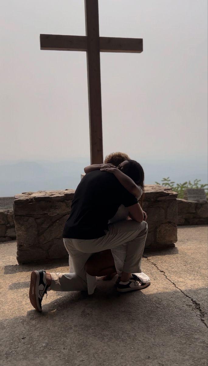 a man kneeling down in front of a cross on top of a stone wall with his hands over his face