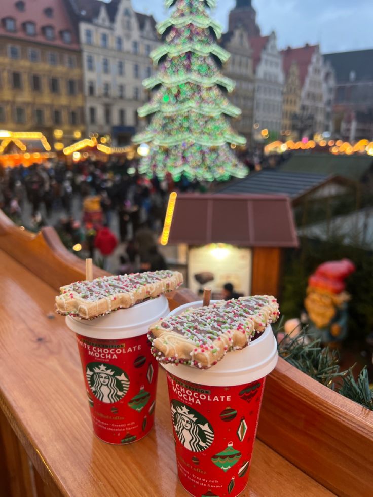 two cups of coffee sitting on top of a wooden table next to a christmas tree