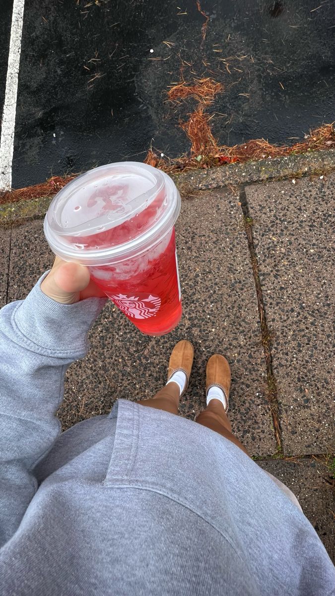 a person holding up a plastic cup with red liquid in it on the sidewalk next to a street