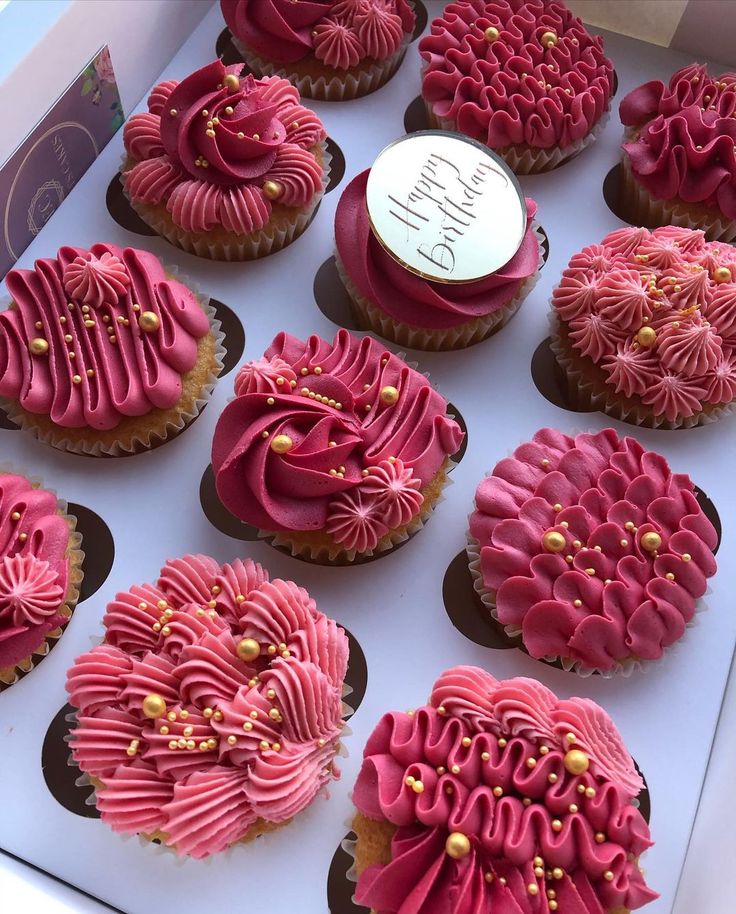 twelve pink cupcakes in a box with gold decorations on the top and bottom