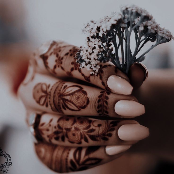 a woman's hands with henna and flowers on their fingers, holding something in her hand