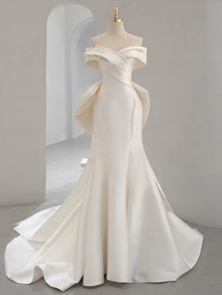 Draped in luxurious ivory satin, this stunning mermaid gown radiates elegant simplicity and modern refinement. The strapless neckline flows seamlessly into a pleated and gathered bodice, enhancing the natural curves of the wearer's figure. A large bow accentuates the back of the dress, which features a zipper closure. The floor-length skirt fits snugly through the hips and thighs before flaring out into a dramatic train, creating a bold and striking silhouette. Long White Wedding Dress, Light Wedding Dresses, Fishtail Wedding Dress, Wedding Entrance, Mermaid Gown, Fairy Dress, Wedding Outfits, White Wedding Dresses, Wedding Dress Styles