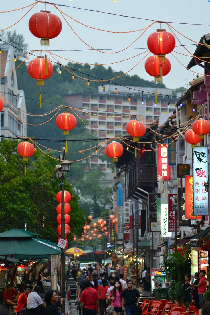 many red lanterns hanging from the side of buildings and people walking down a city street