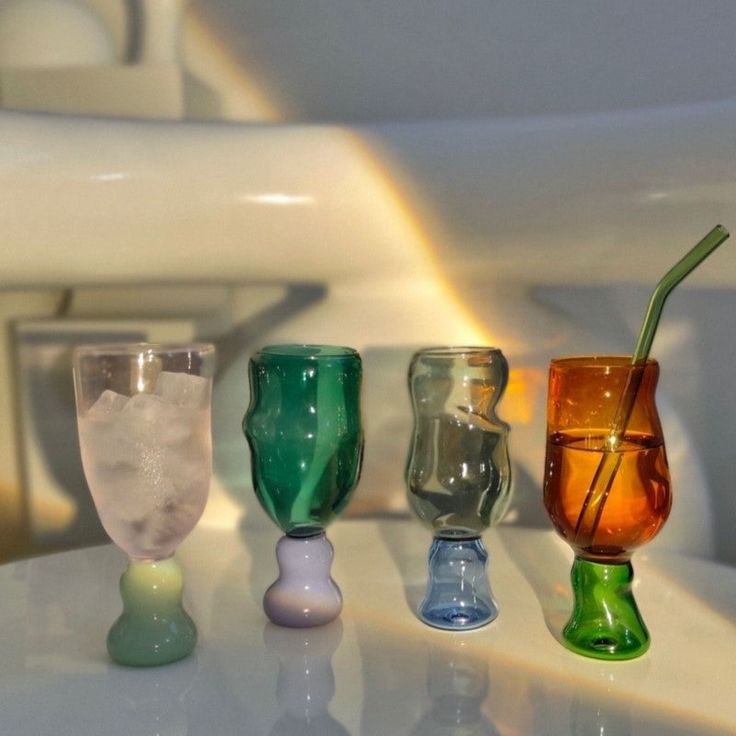 three different colored glasses sitting on top of a white table next to a toilet bowl