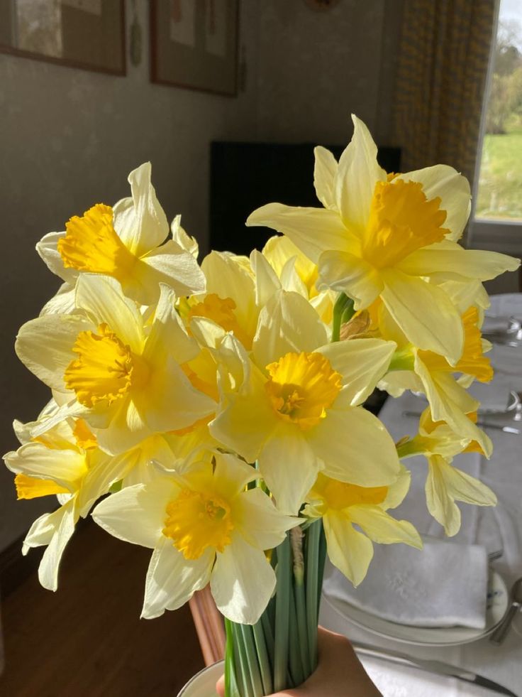 a vase filled with yellow daffodils on top of a wooden table next to a window