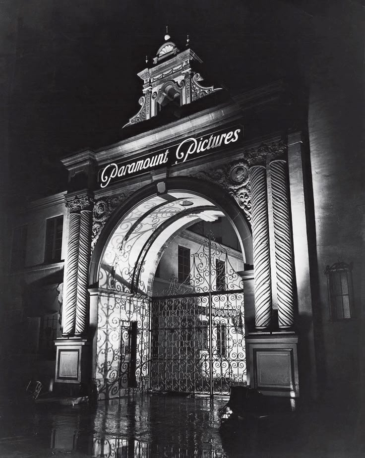 black and white photograph of an entrance to a building at night with the words paramount pictures on it