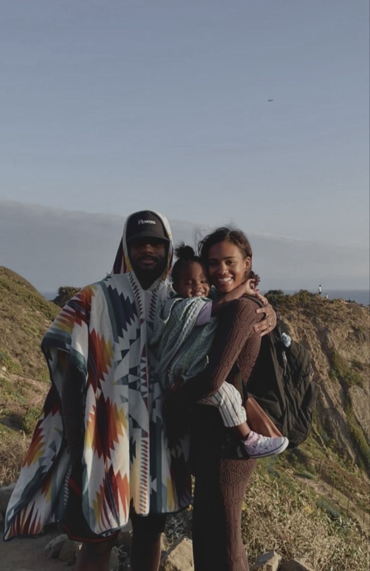 a man and woman standing on top of a hill with a baby in their arms