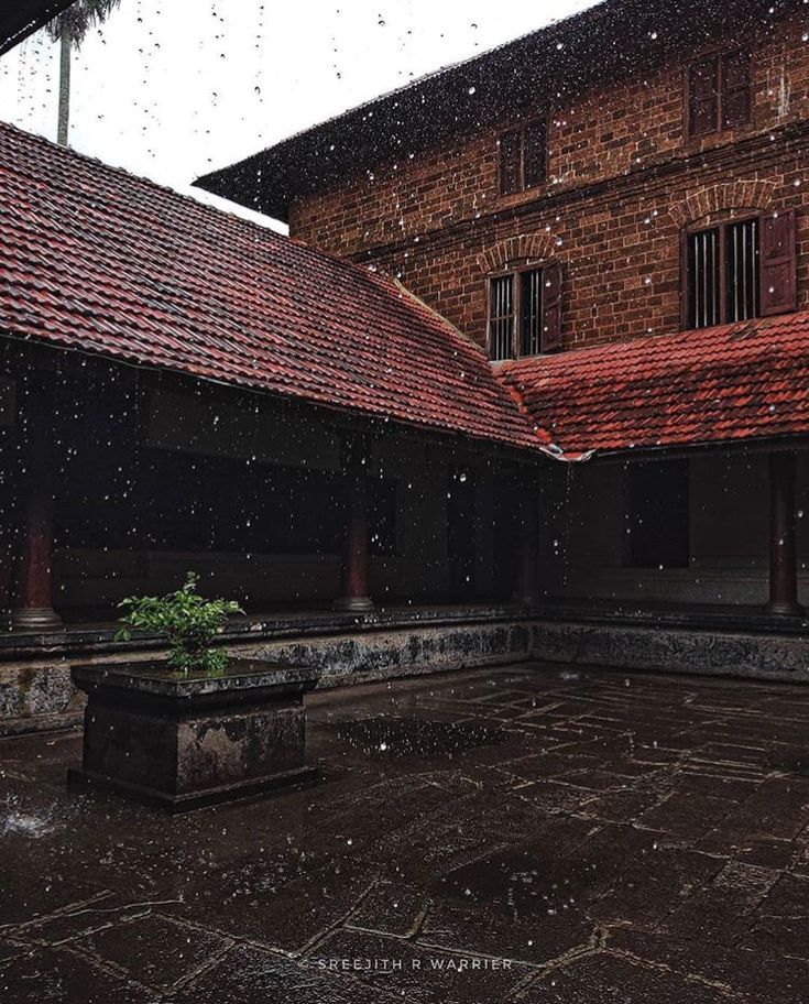 an old building with red tile roofing and brick walls is shown in the rain