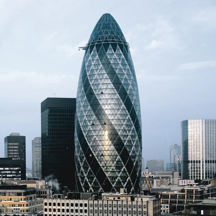 a very tall glass building in the middle of a city with other buildings around it