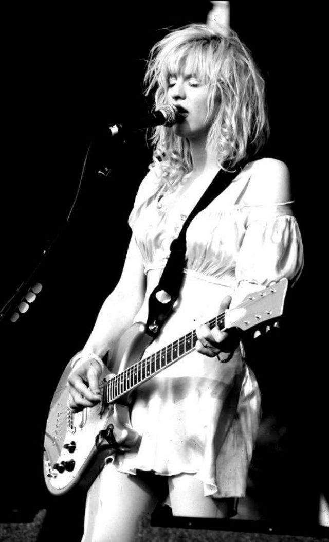 a black and white photo of a woman singing into a microphone while holding a guitar