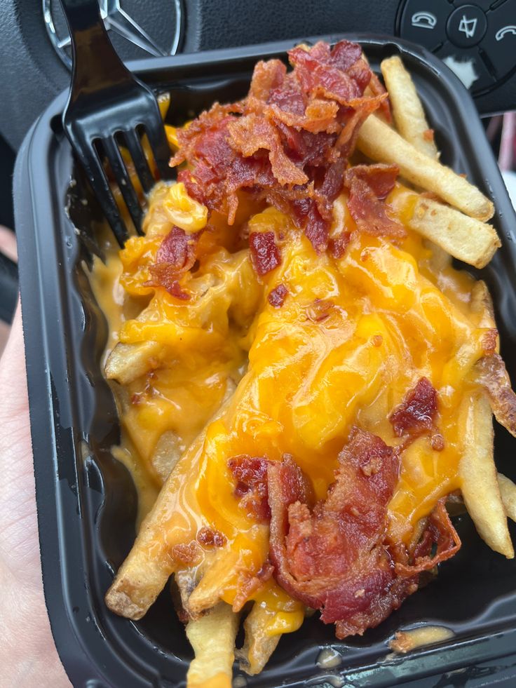 a plastic container filled with french fries covered in cheese and bacon