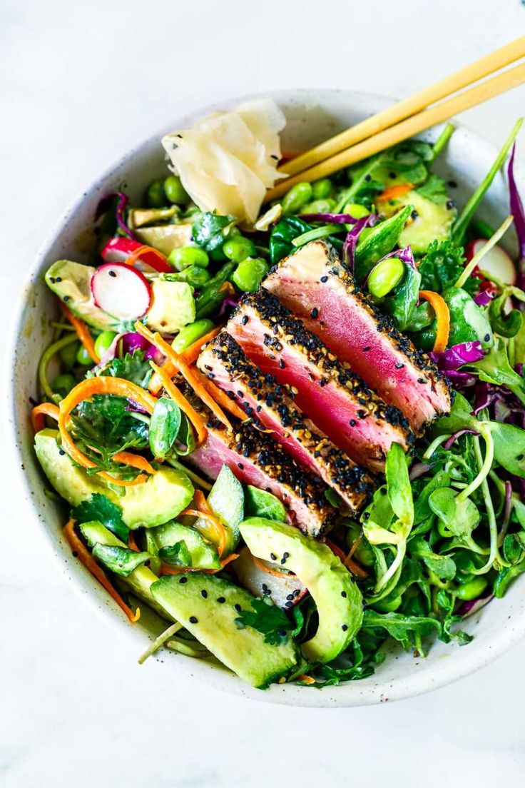 a white bowl filled with meat and veggies next to two chopsticks