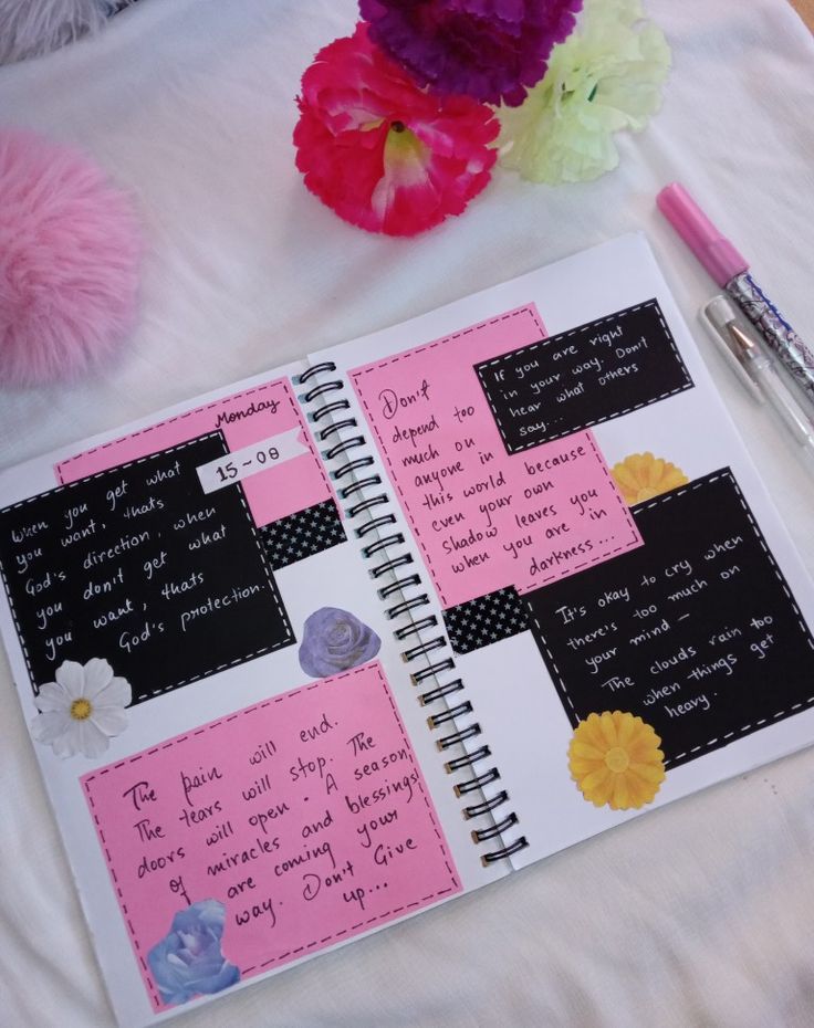 a pink and black notebook with writing on it next to some colorful flowers, two pens and a teddy bear