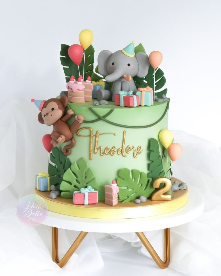 a birthday cake with an elephant and monkey on top, surrounded by jungle leaves and balloons