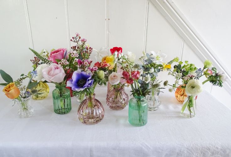 there are many different vases with flowers in them on the white cloth tablecloth