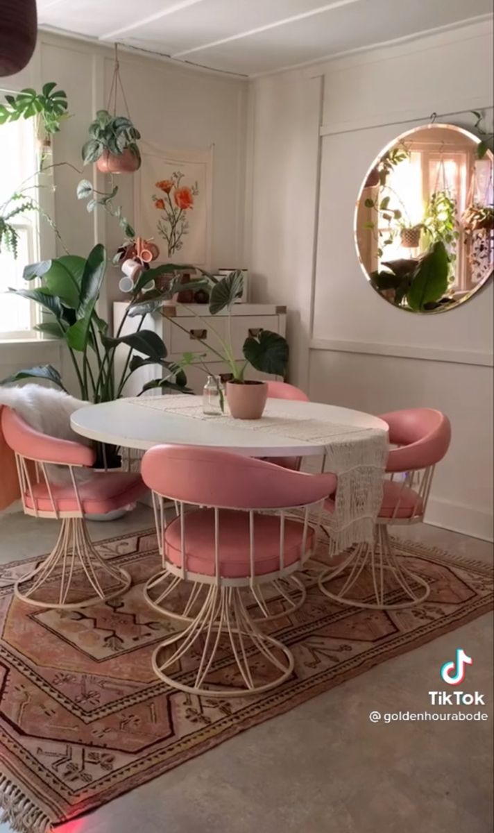 a dining table with pink chairs and potted plants in the corner next to it