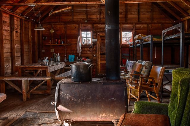 an old fashioned stove in the middle of a room with wooden floors and walls, surrounded by furniture