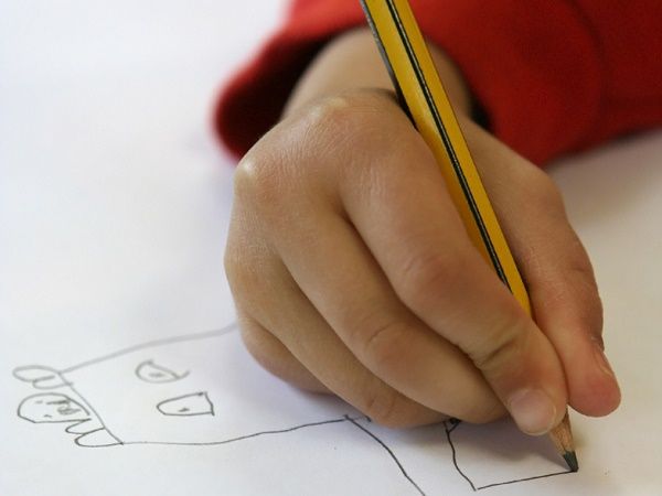 a child's hand holding a pencil while drawing on paper