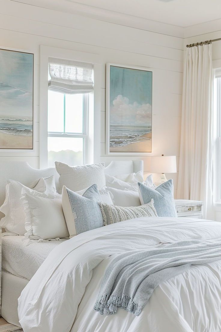 a bedroom with white bedding and paintings on the wall