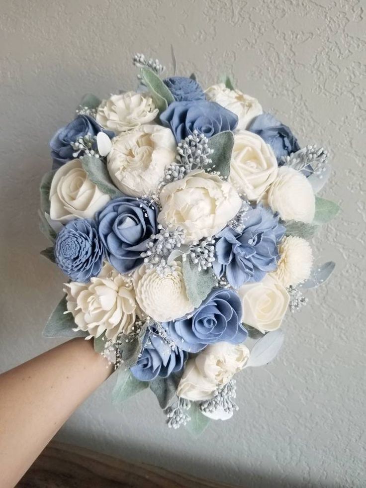 a bridal bouquet with blue and white flowers is being held by someone's hand