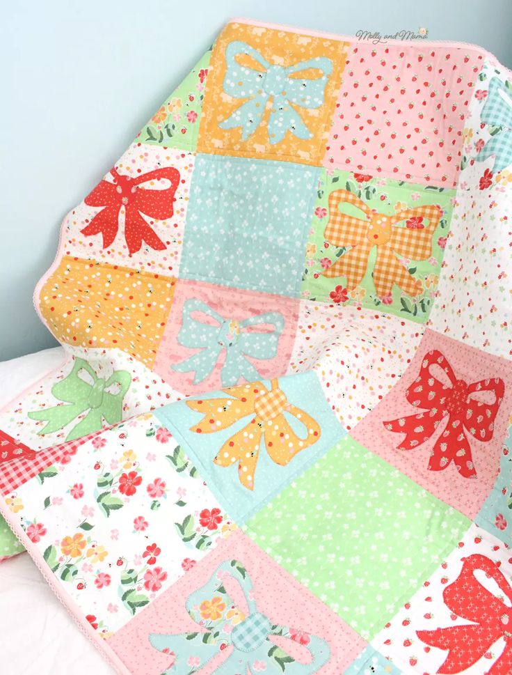 a baby quilt with bows on it is laying on a bed in a room that has blue walls