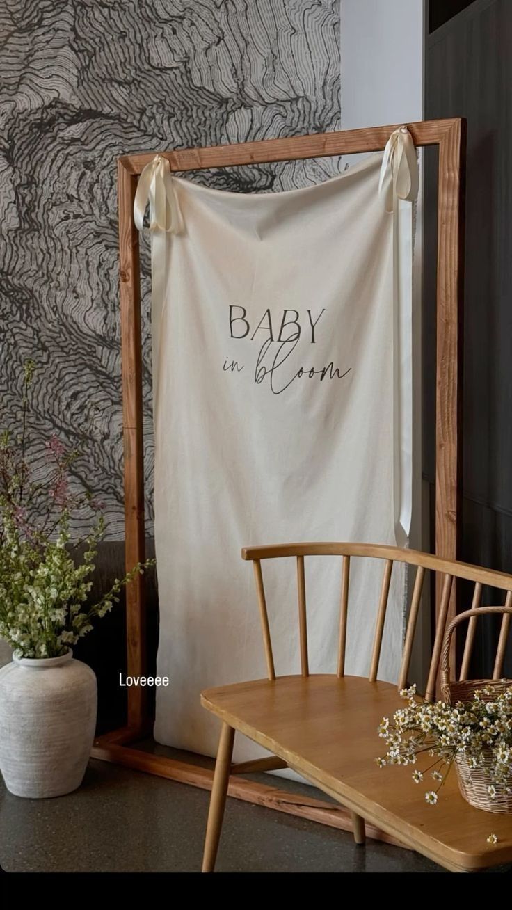 a wooden chair sitting next to a table with a baby in bloom banner on it