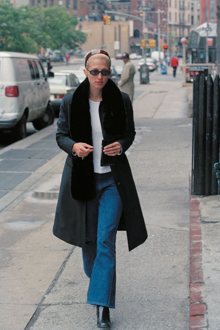 a woman walking down the street wearing jeans and a coat