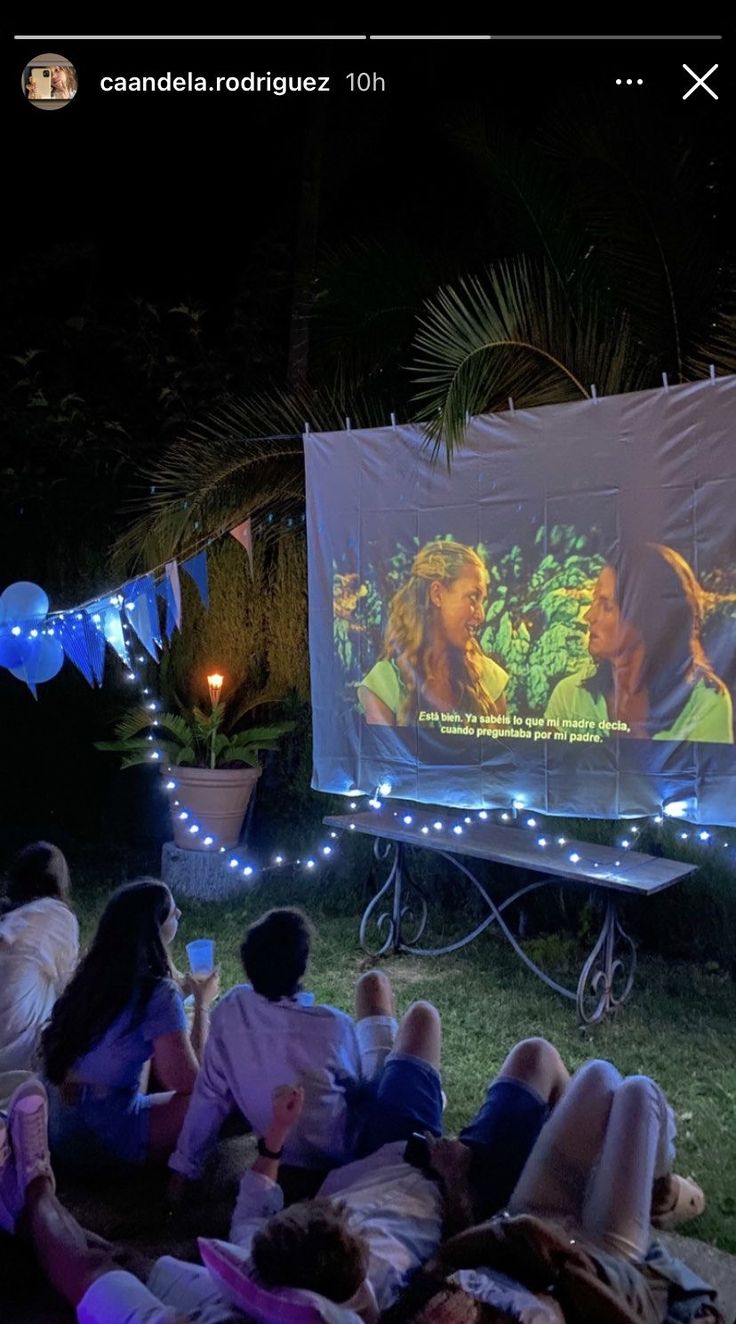 people sitting in the grass watching a movie on an outdoor projector screen at night