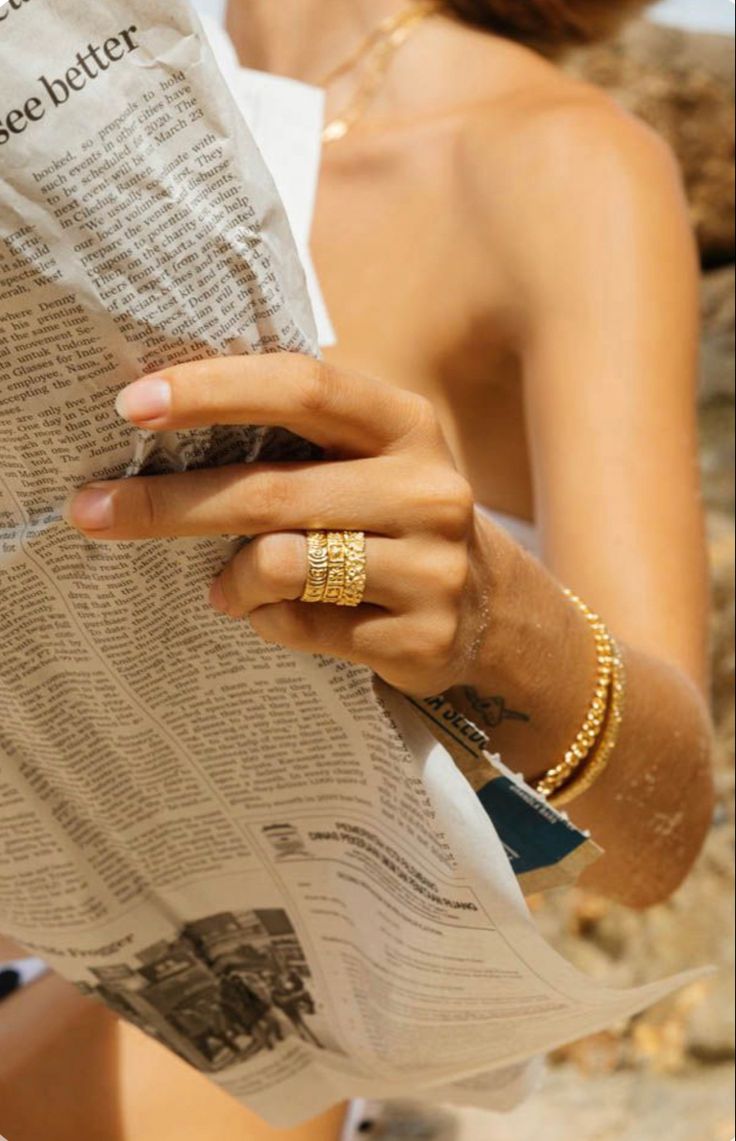 a woman reading a newspaper with her hand on top of the paper and holding it