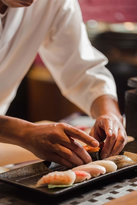 a person is preparing sushi on a tray in a restaurant or bar, with chopsticks sticking out of it