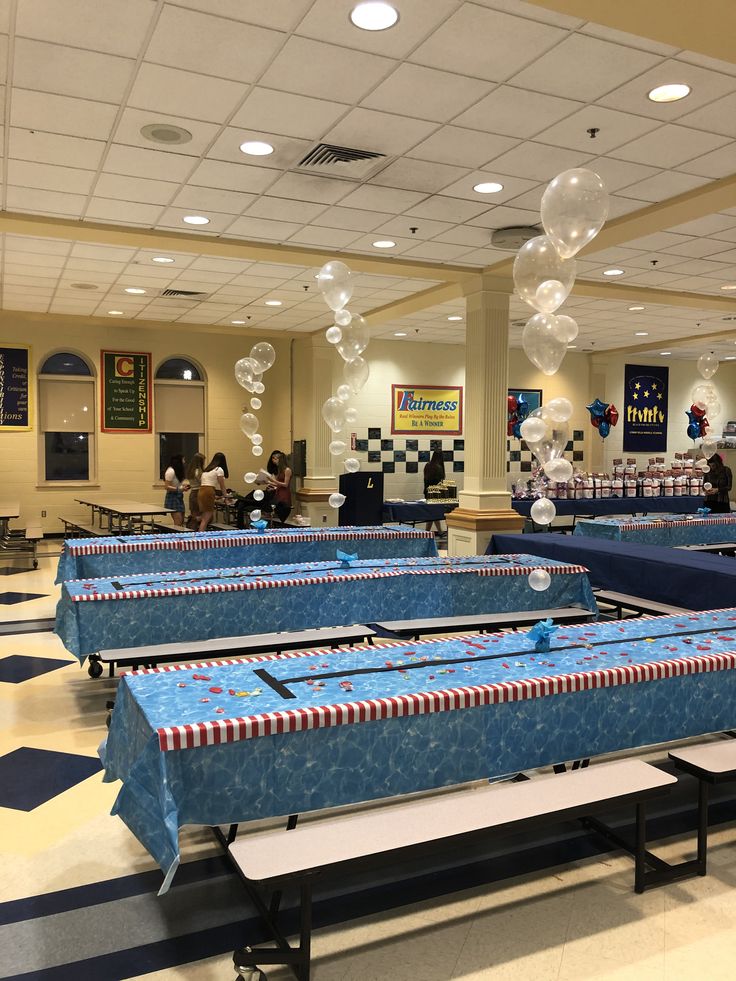 several tables with blue covers and balloons floating in the air at a school banquet hall