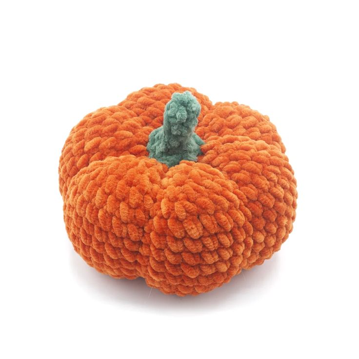 an orange knitted pumpkin sitting on top of a white surface with a green stuffed animal in the middle