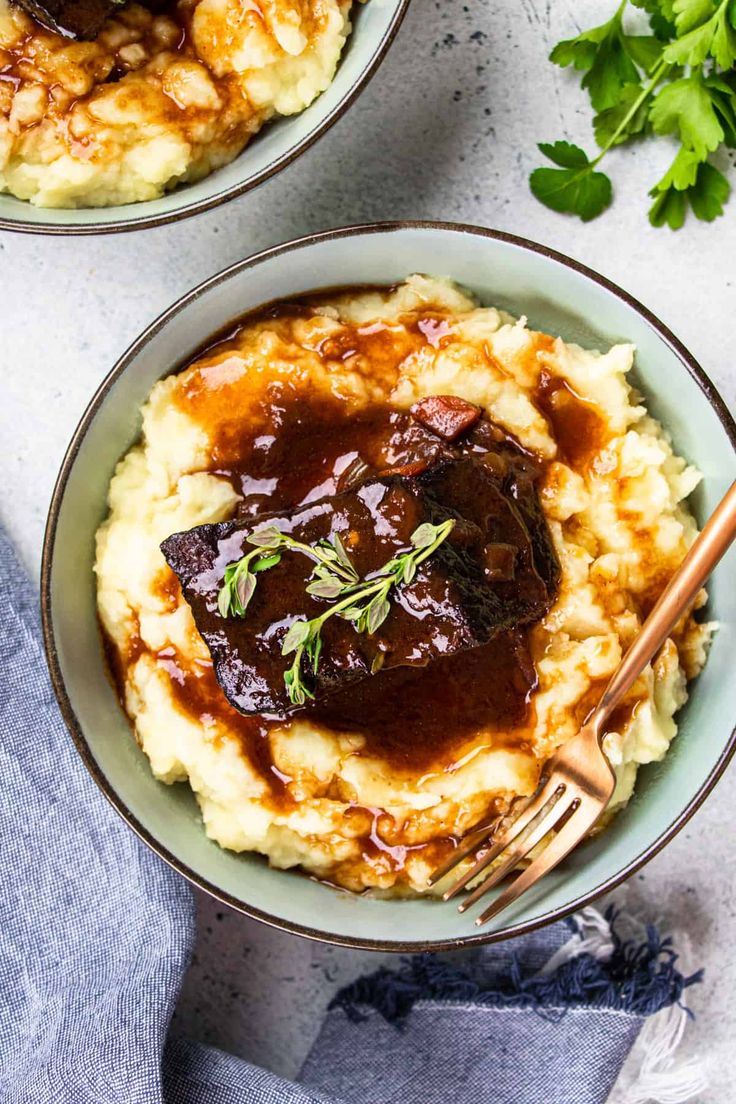 two bowls filled with mashed potatoes covered in gravy and garnished with herbs